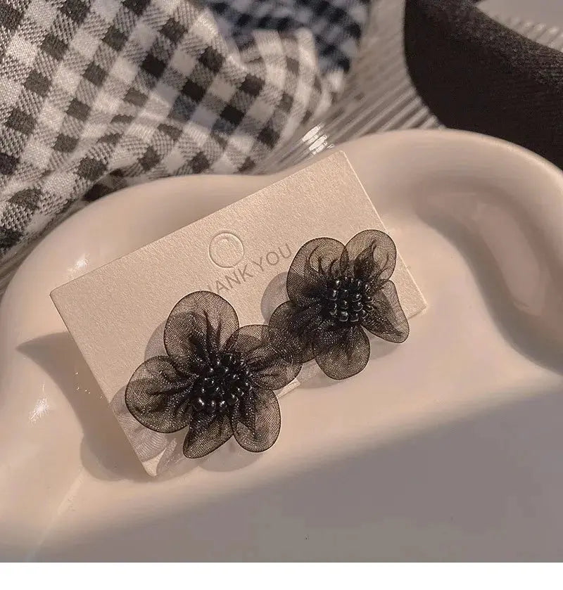 Two black enamel flower earrings on a white display card