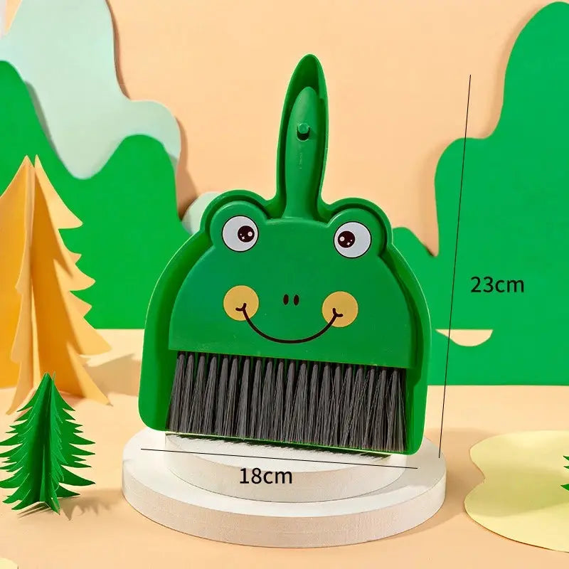 Mini frog-shaped desktop broom, green plastic with black bristles, 18 cm wide, 23 cm tall.