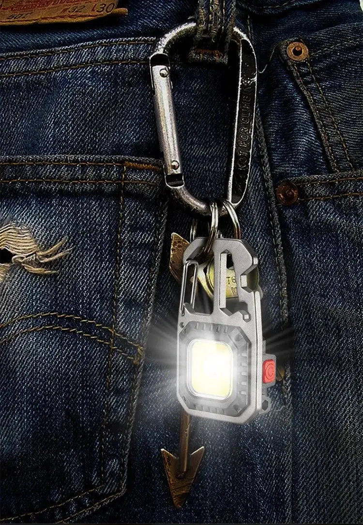 COB keychain work light with battery display, aluminum body, red power button, attached to carabiner on denim jeans.