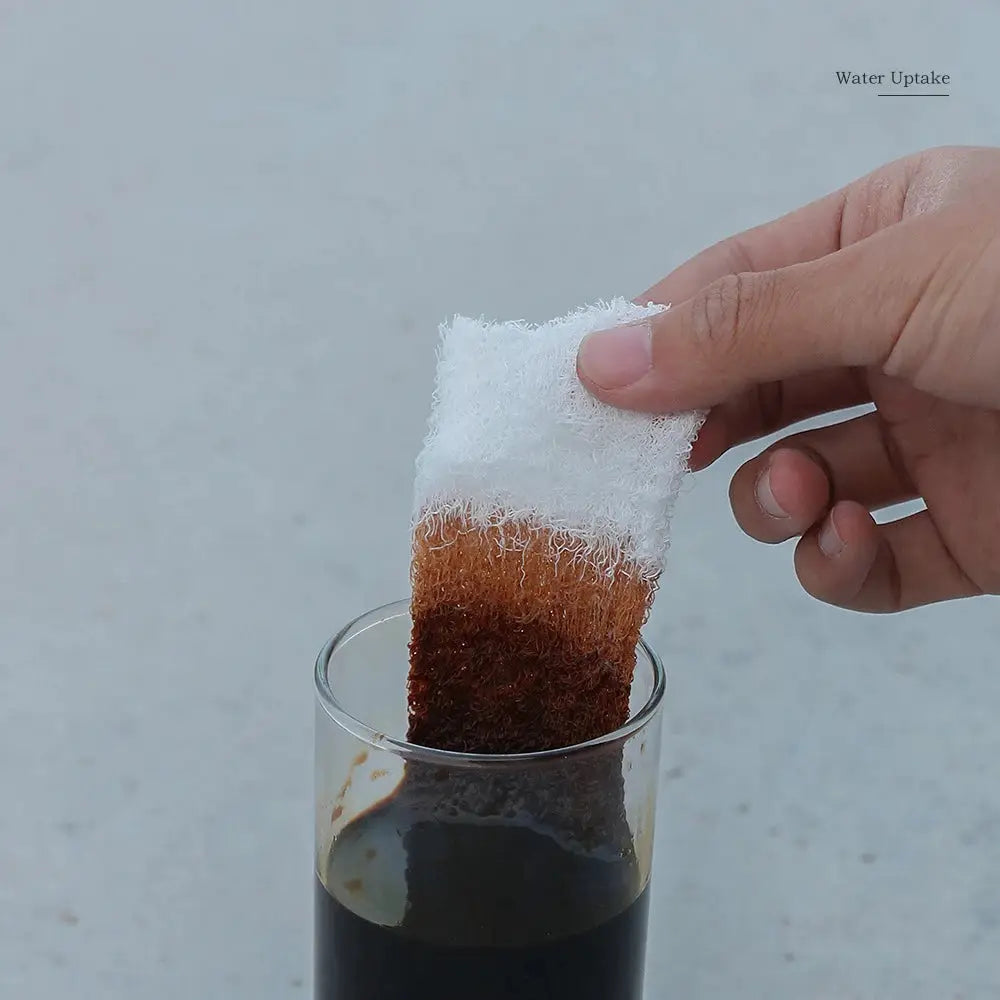 First aid compressed sterile gauze roll, white, Z-folded, being dipped into dark liquid in a glass