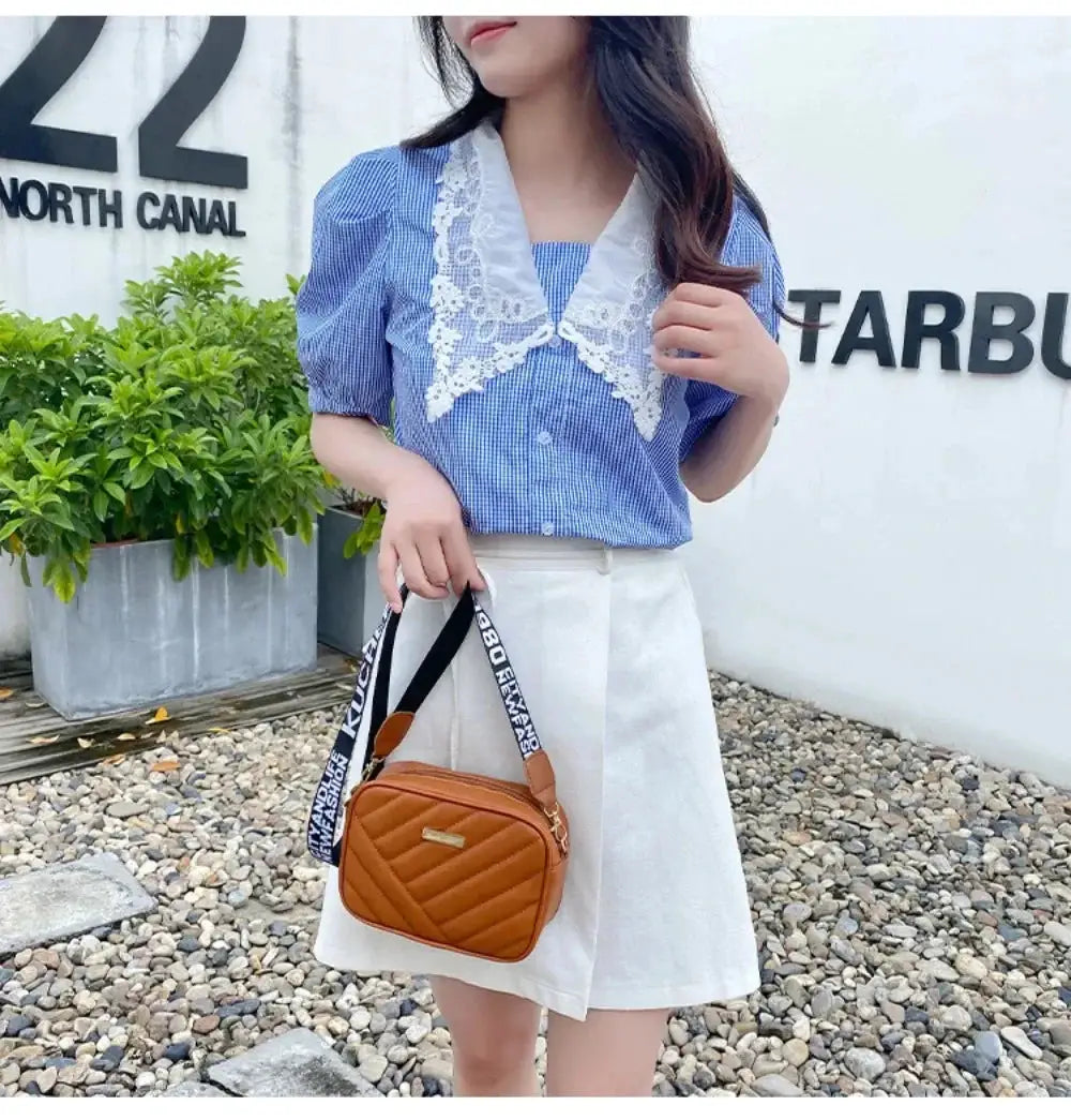 Shoulder bag tan quilted PU with a black-and-white strap, held by a woman in a blue top and white skirt