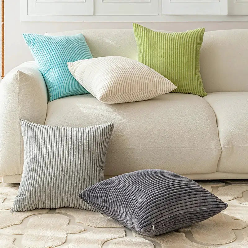 Corduroy pillow covers on beige sofa in blue, cream, lime green, gray and charcoal; five cushions.