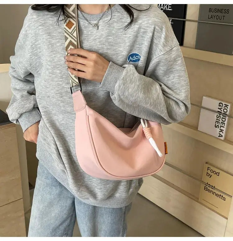 Pink dumpling-style crossbody bag with a wide patterned shoulder strap worn with a gray oversized sweatshirt
