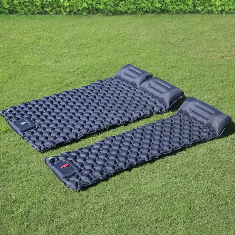 Two navy blue camping air mattresses with built-in head pillows on a green lawn.