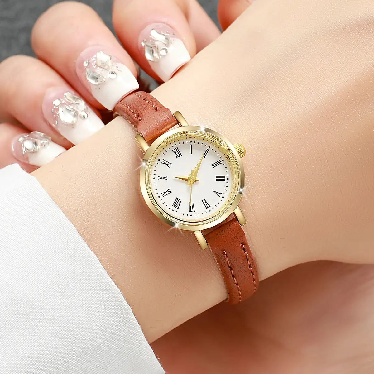 Women's watch with brown leather strap, gold-tone case, white dial with Roman numerals.