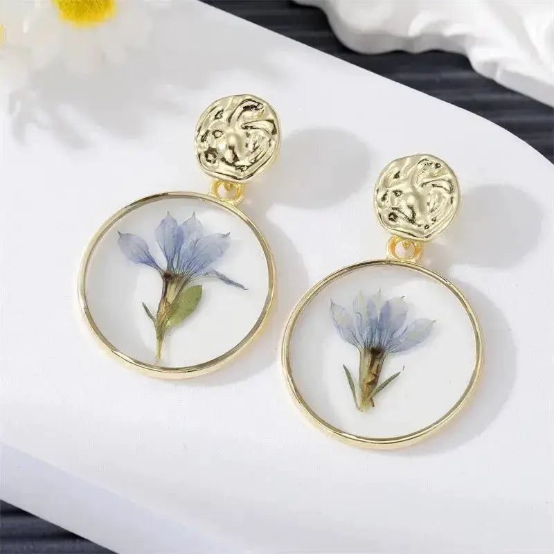 Gold-tone drop earrings with circular resin hoops housing blue pressed flowers, pair