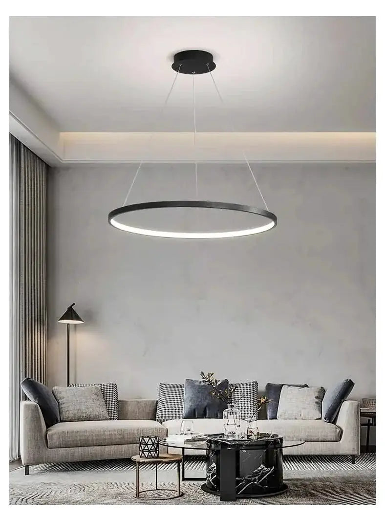 Modern round LED pendant light with a black ring and white glow, suspended over a gray living room.