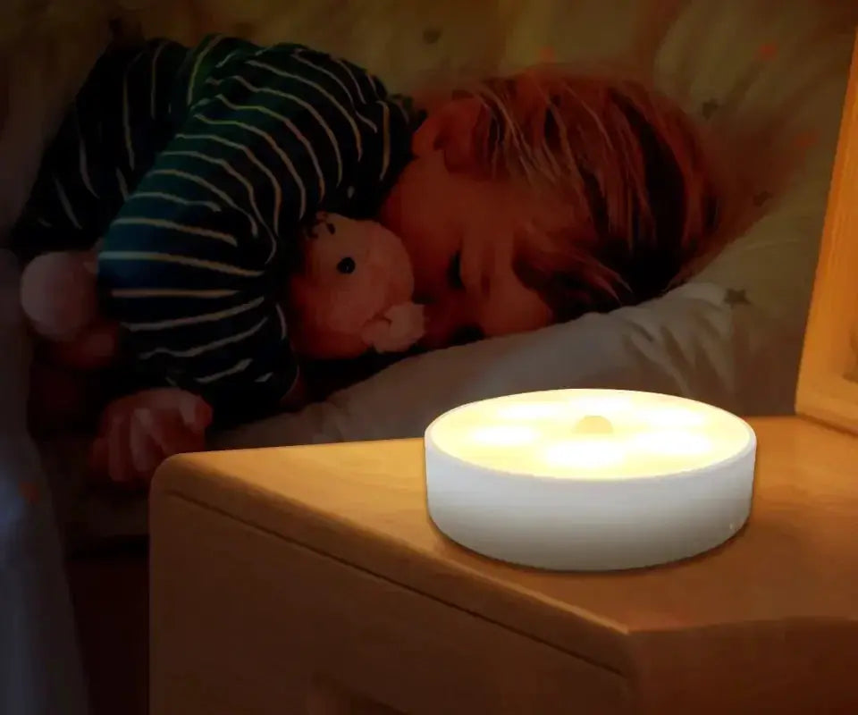 LED motion sensor night light, round white plastic, warm glow on bedside table with sleeping child