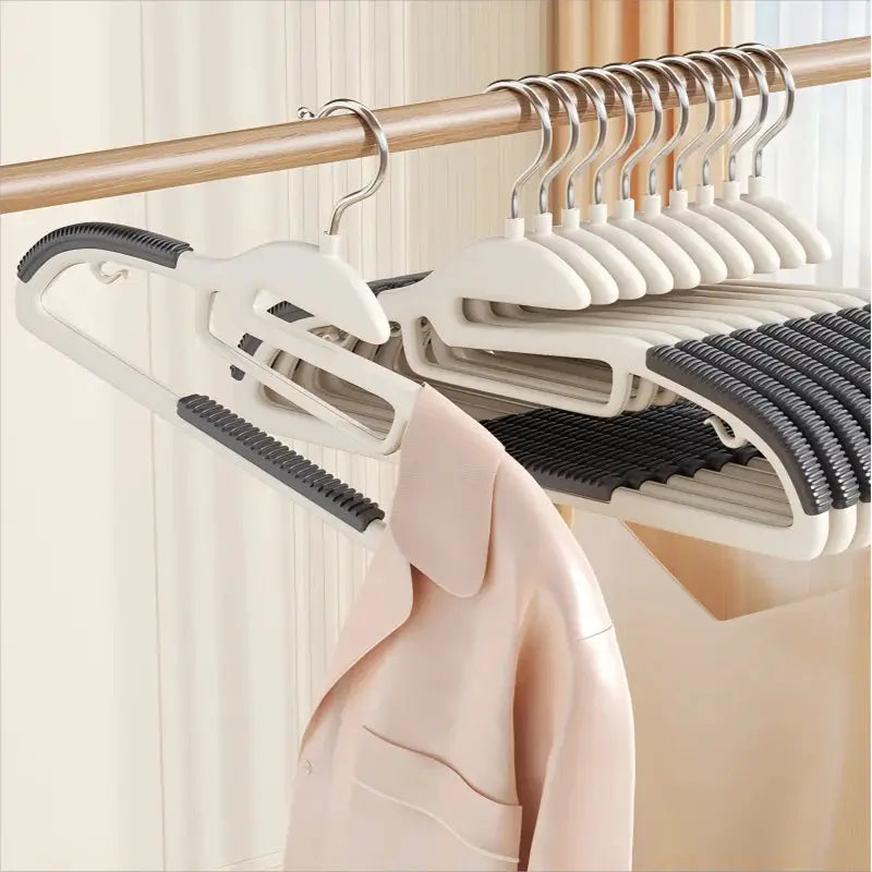 10-pack multifunctional wet-dry clothes hangers in white with black anti-slip grips on wooden rod, holding a pink blouse