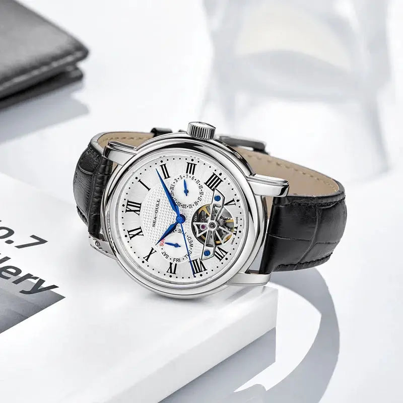 Men's automatic mechanical wristwatch with silver case, white Roman-numeral dial, blue hands, black leather strap.