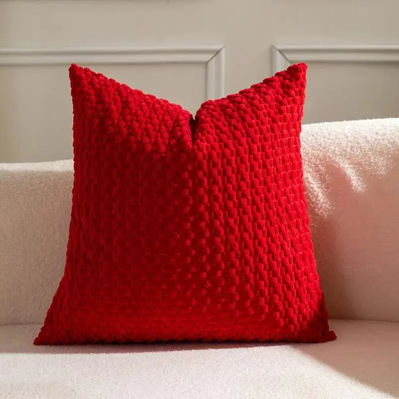 Red velvet cushion with textured surface on a pale pink sofa.