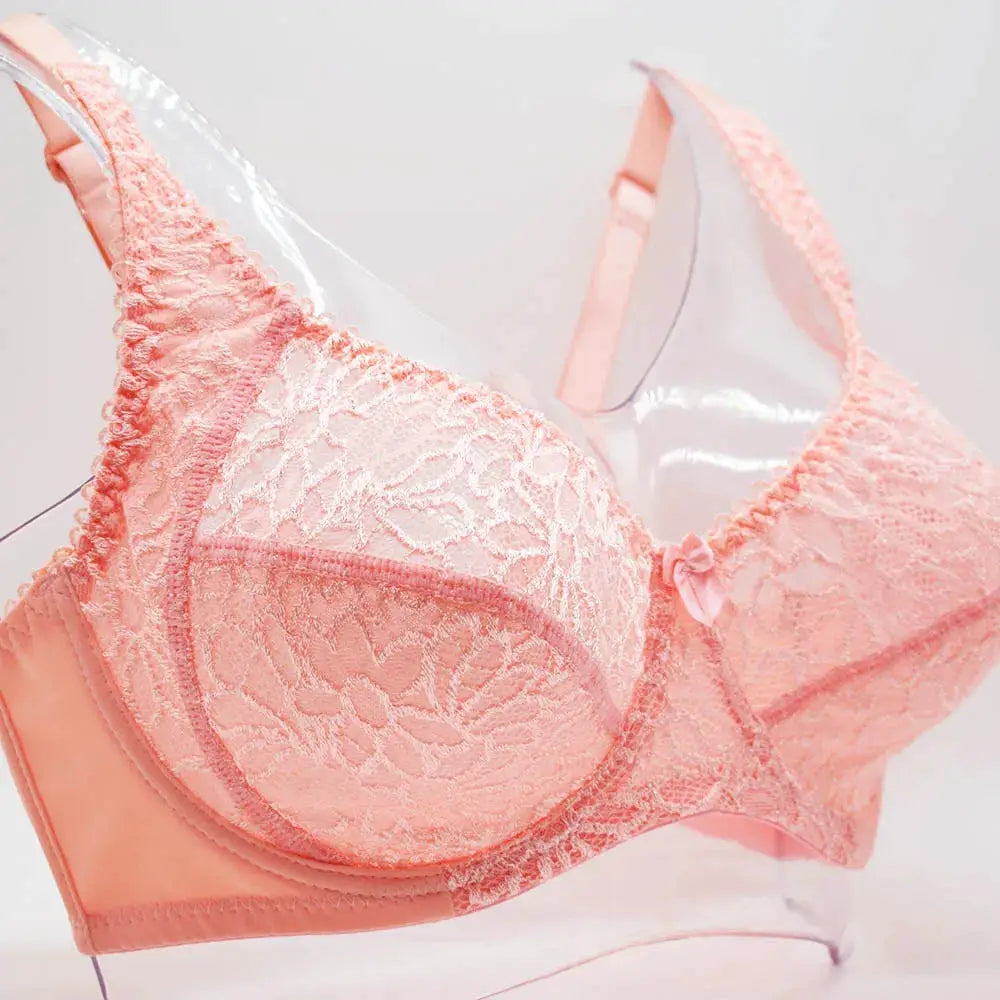 Plus-size pink lace underwire bra with floral pattern, scalloped edges, satin bow center, soft pastel lingerie.