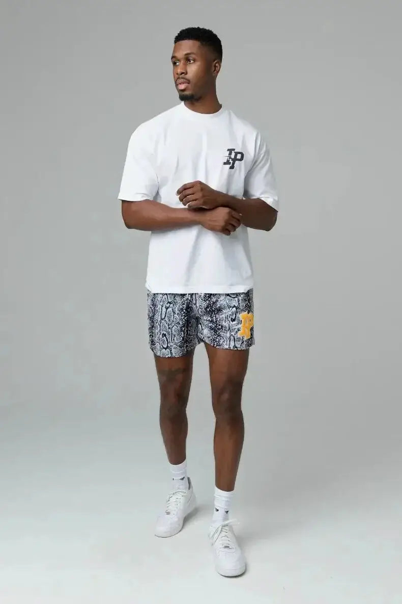 Men's shorts with snakeskin print and yellow emblem, paired with a white T-shirt and white sneakers.