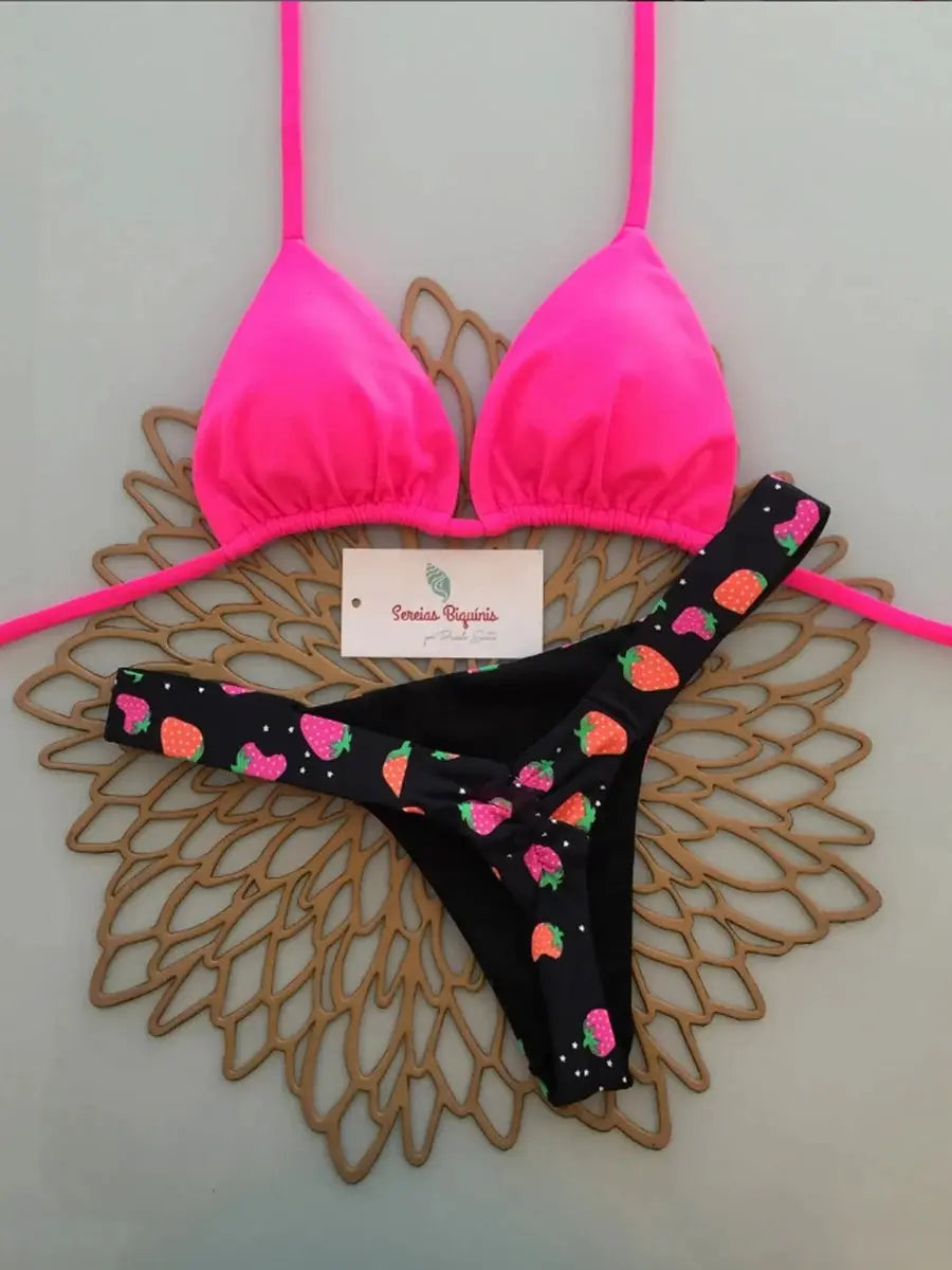 Two-piece bikini set: neon pink halter triangle top with string straps and black thong bottom with strawberry print.