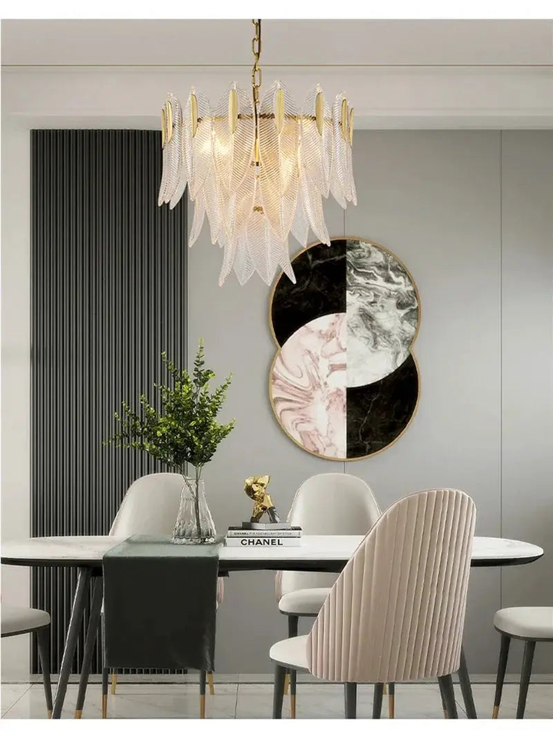 Glass chandelier pendant lamp with leaf-shaped clear glass panels and a brass chain over a dining table.