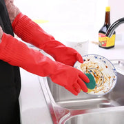 Silicone dishwashing gloves, red long-length pair, used to scrub a plate at the kitchen sink.