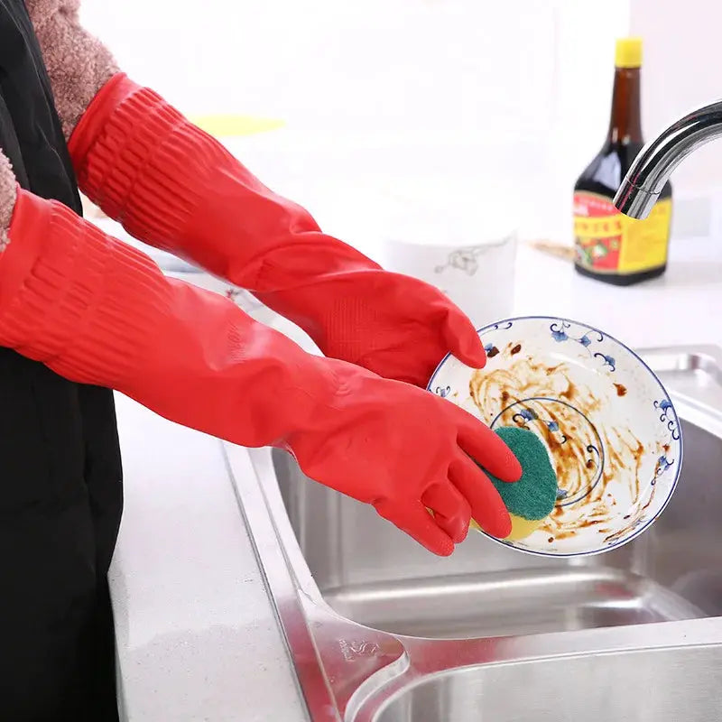 Silicone dishwashing gloves, red long-length pair, used to scrub a plate at the kitchen sink.