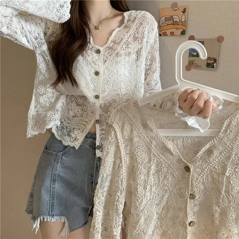 Floral white lace blouse with sheer long sleeves, scalloped edges, button-front; paired with denim shorts.