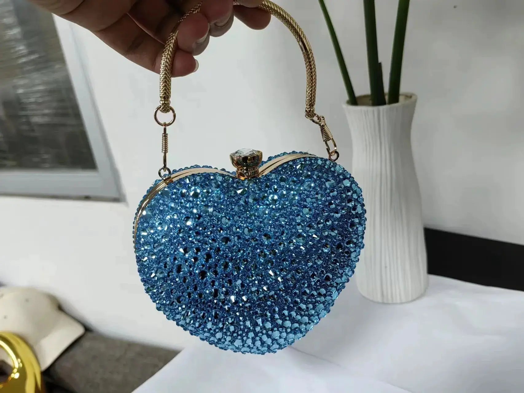 Blue heart-shaped crystal clutch with gold-tone frame and rhinestone-studded body.