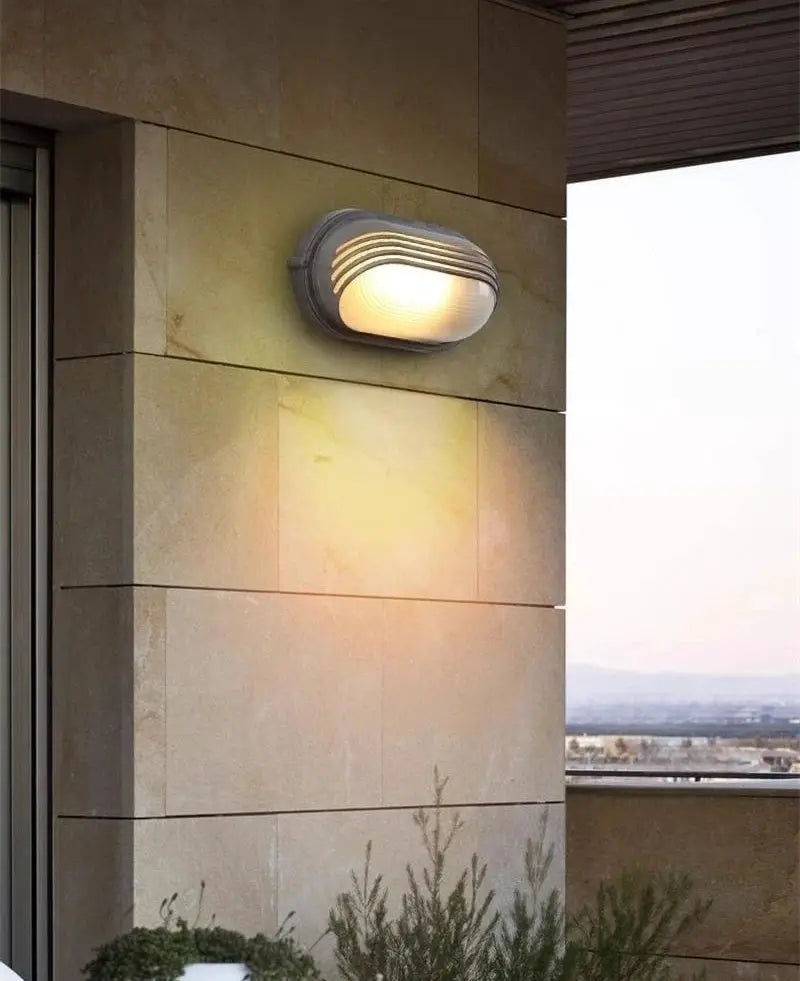 Outdoor retro LED wall lamp with glass diffuser and gray metal housing, mounted on a stone exterior wall.
