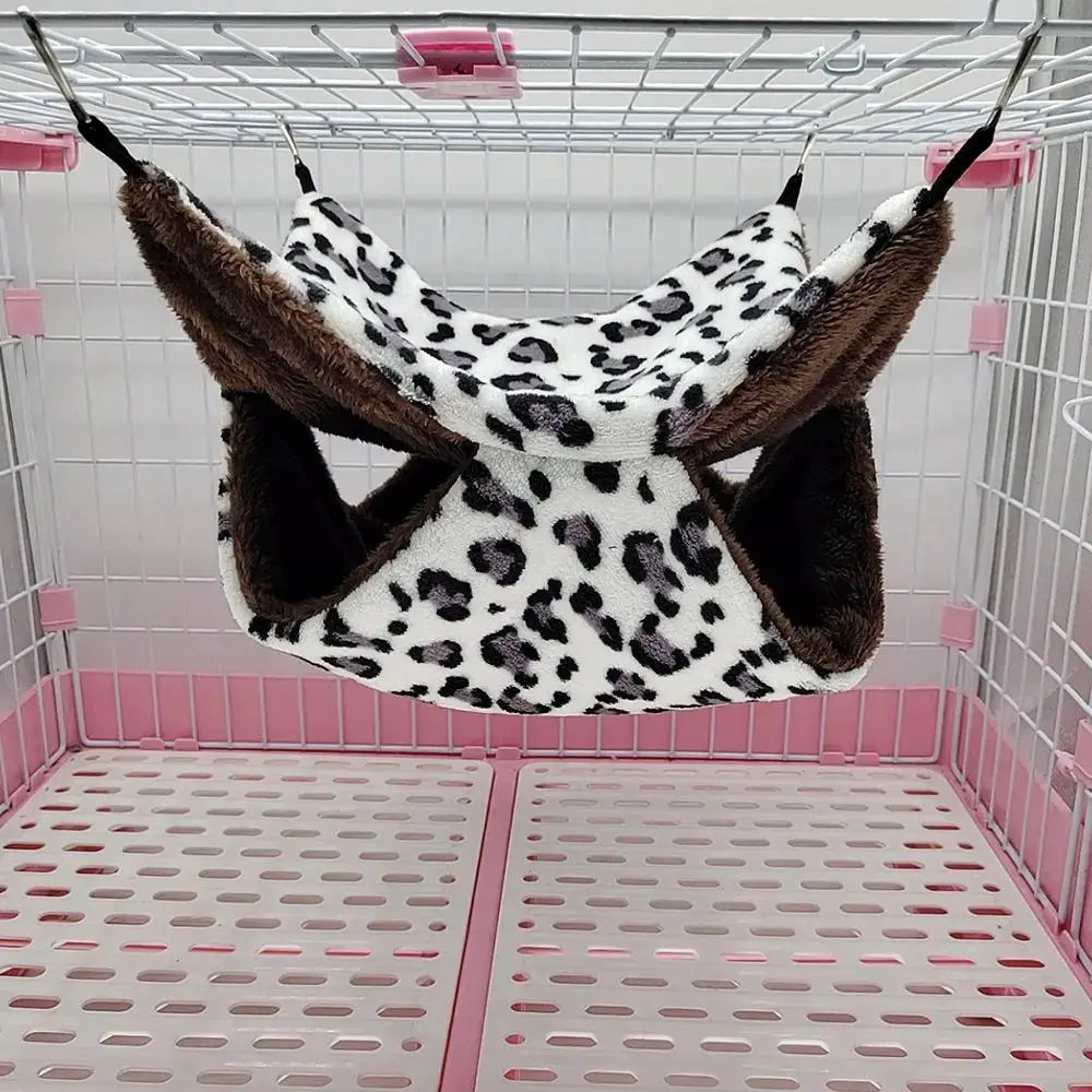 Warm plush hamster hammock with leopard print and brown lining, hanging in a small animal cage.