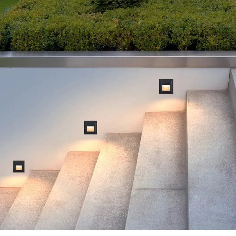 LED wall lights: four square black recessed stair lights along outdoor stone steps emitting warm glow