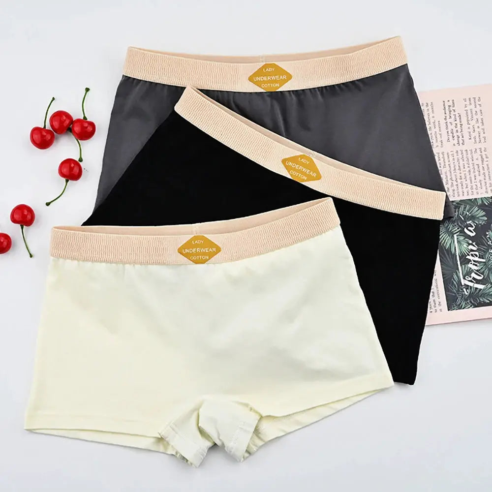 Three-pack women's cotton boxer shorts in cream, black, and pale yellow with peach elastic waistbands