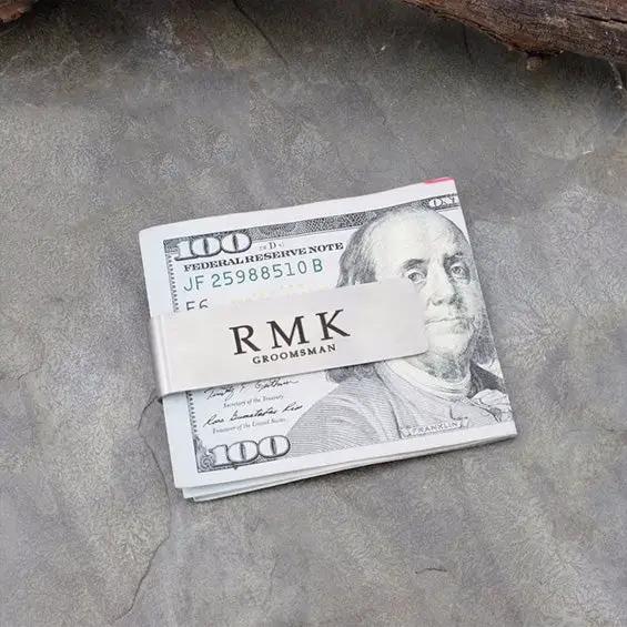 Personalized money clip engraved RMK GROOMSMAN in silver metal with a stack of hundred-dollar bills