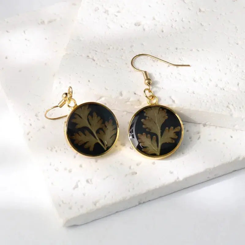 Earrings: Simples Market pair of round gold-framed epoxy resin earrings with black background and pressed leaf design