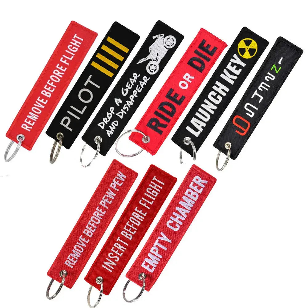 Set of 10 embroidered fabric key fobs with metal rings in red and black, featuring Remove Before Flight and Ride or Die