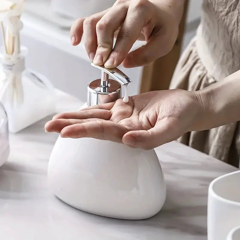 Soap dispenser, white ceramic with chrome pump, on marble bathroom counter.