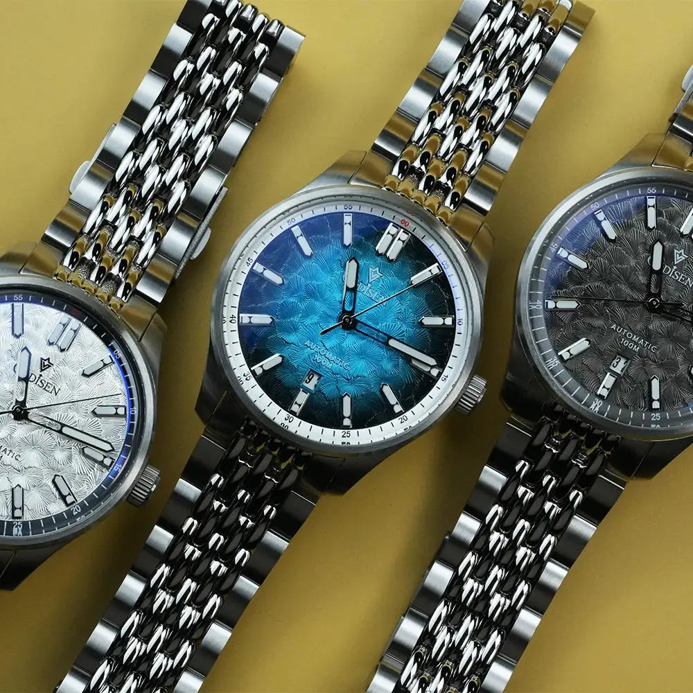 Three CADISEN 2026 automatic men's watches on stainless steel bracelets with blue, white, and gray patterned dials
