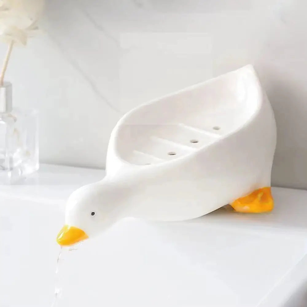 Duck-shaped self-draining soap tray, white ceramic with yellow beak and feet, Simples Market.