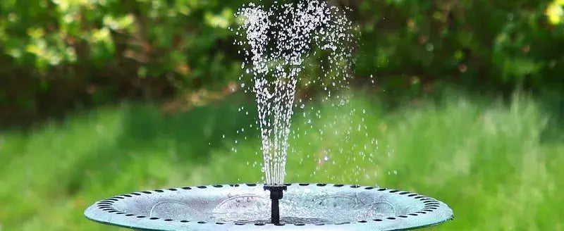 Outdoor solar fountain pump on a metal disc base with a central nozzle spraying water for a garden pond.
