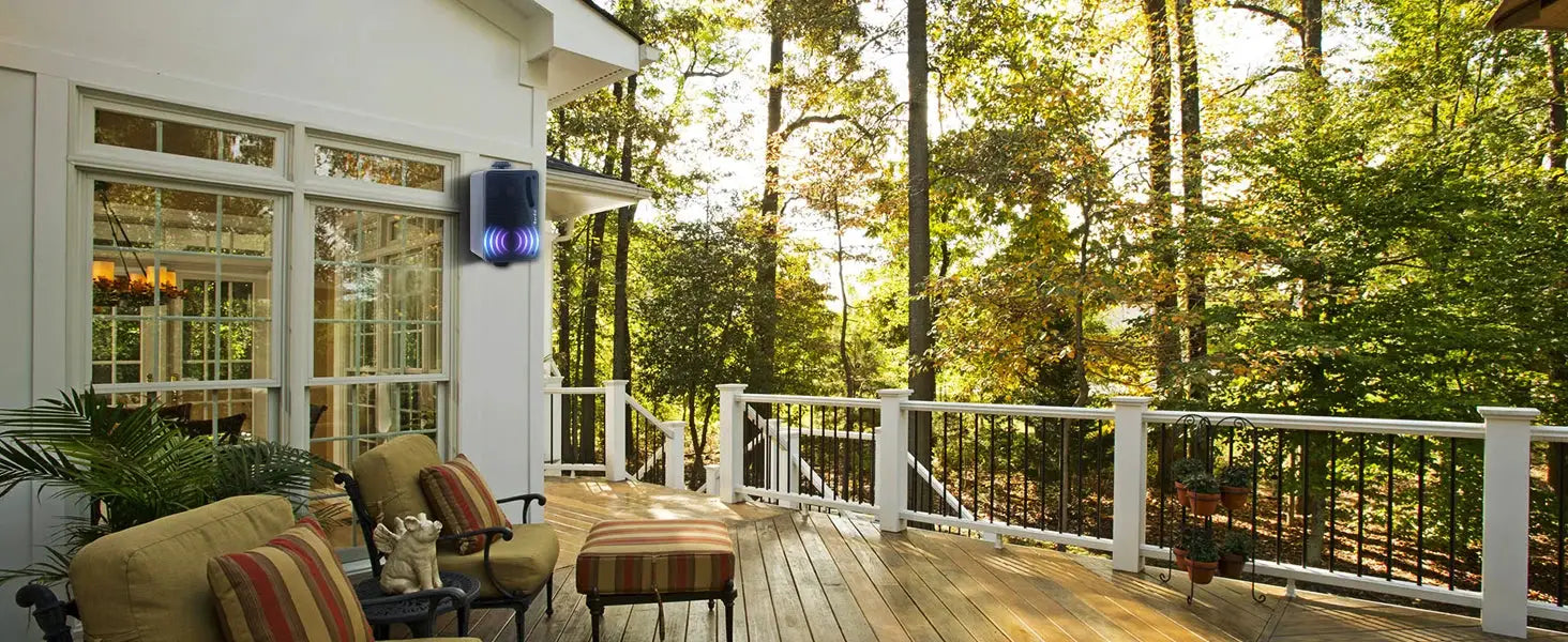 Outdoor wall-mounted Bluetooth speaker on a white house exterior deck, black enclosure with purple glow.