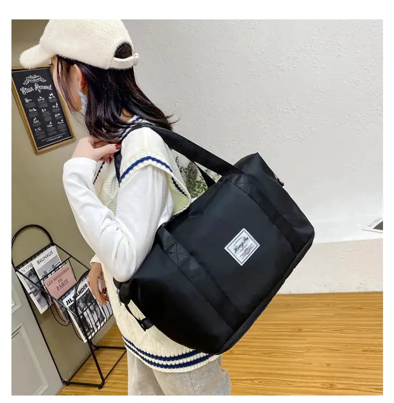 Black nylon carry-on duffle bag with a shoulder strap, large-capacity travel tote carried by a woman.