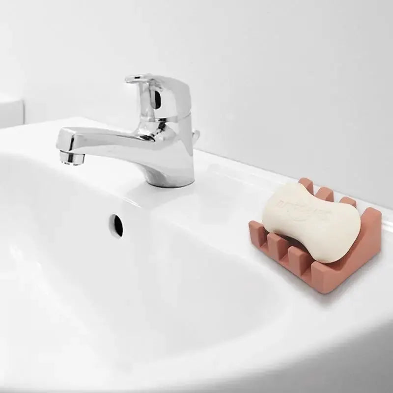 Simples Market silicone soap dish in pink with a white soap bar on a bathroom sink near a chrome faucet