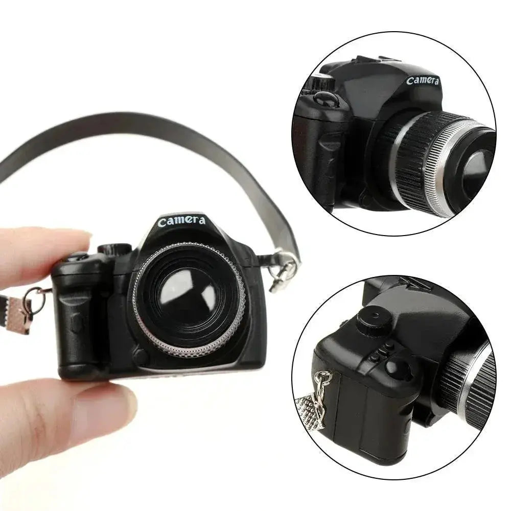 Dollhouse miniature digital SLR camera, black body with silver lens ring and strap.