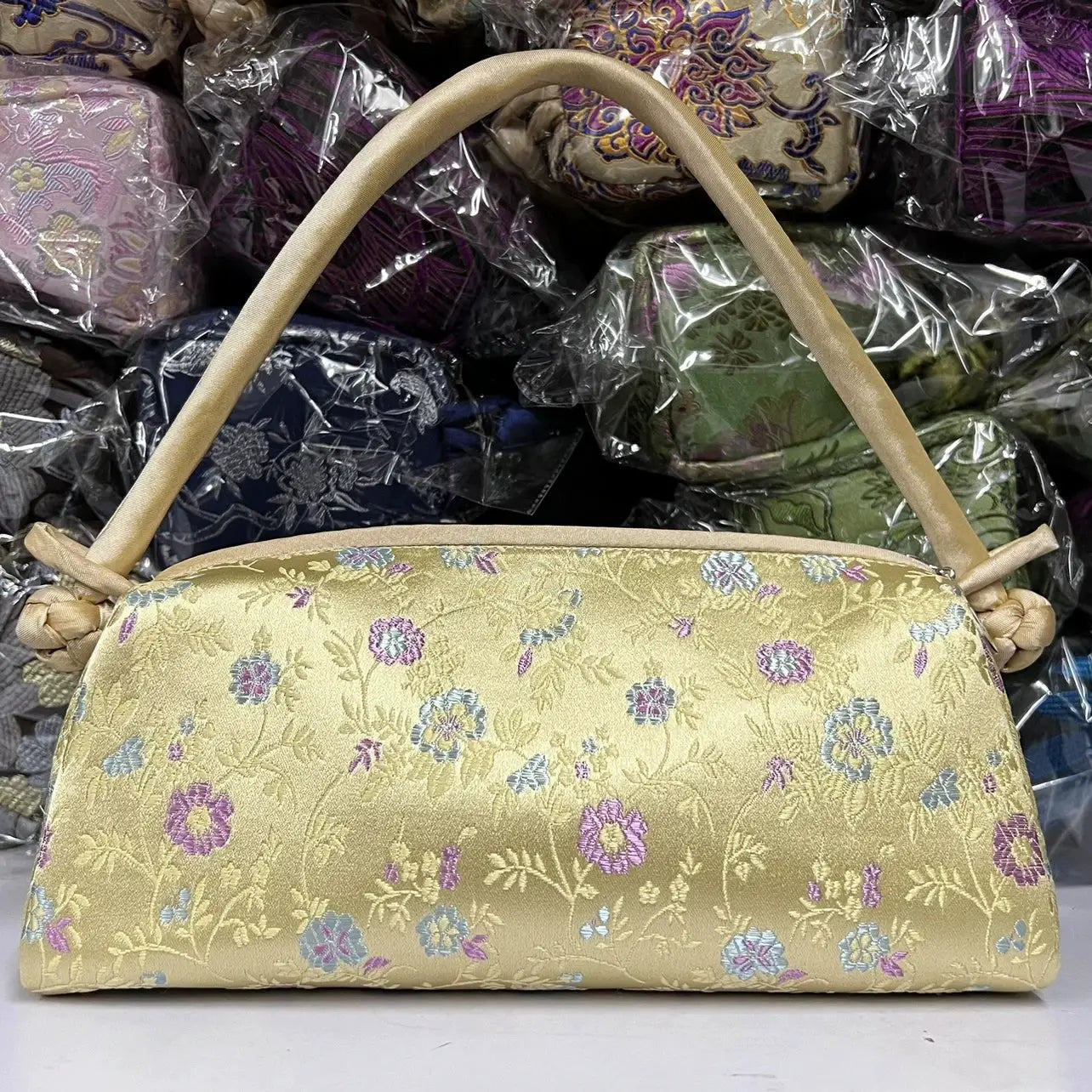 Small gold satin shoulder bag with embroidered floral pattern and knotted handles