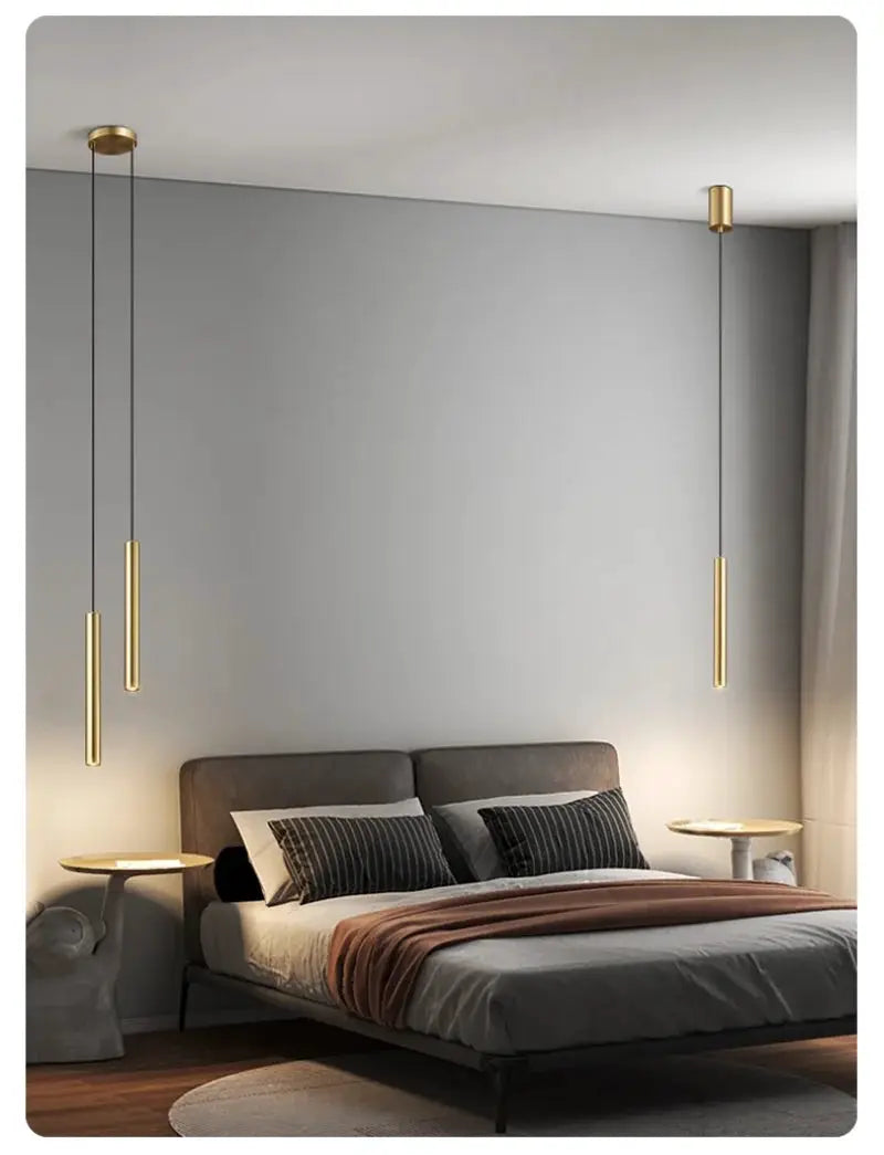 Set of four gold minimalist bedside pendant lamps with cylindrical LED tubes over a gray bedroom with a low platform bed