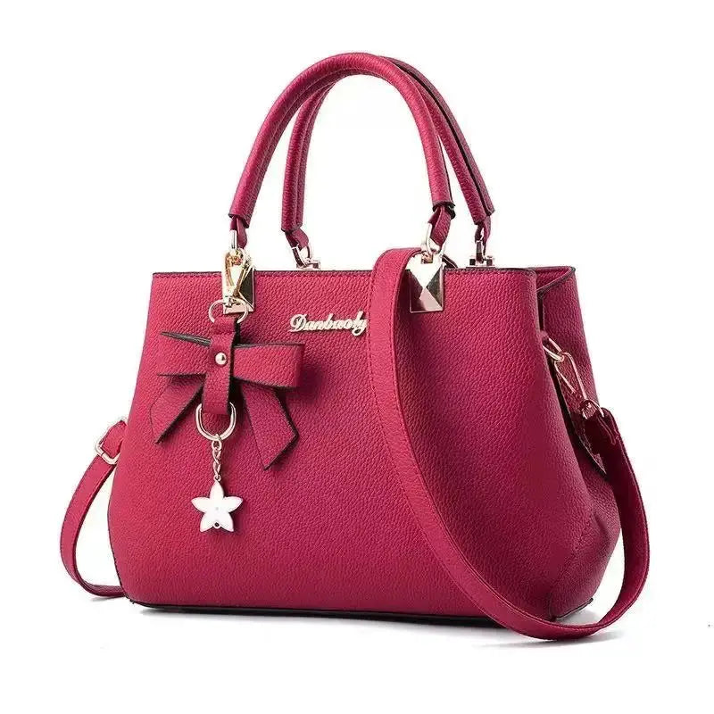 Pink pebbled leather handbag with bow charm, double handles and a detachable crossbody strap