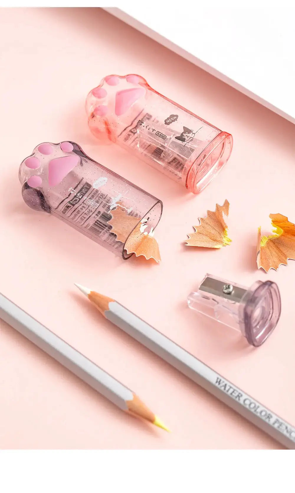 Kawaii cat paw pencil sharpeners, two translucent pink and purple units with shavings.