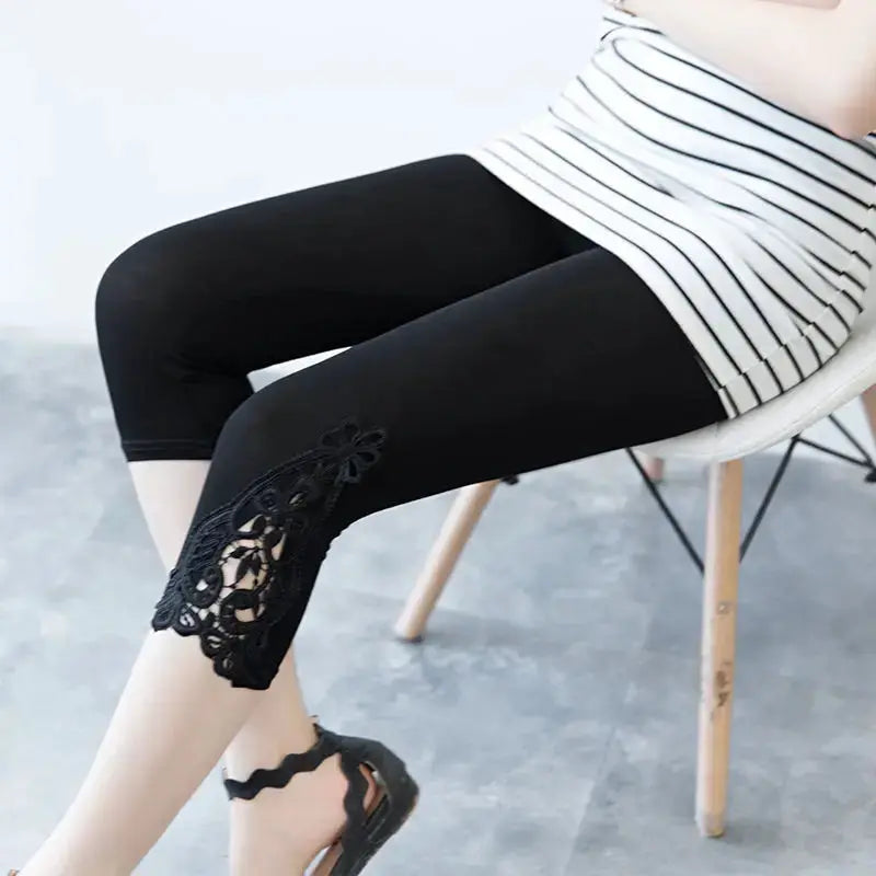 Women's black 3/4 length leggings with lace detail on the lower leg, paired with a striped top.