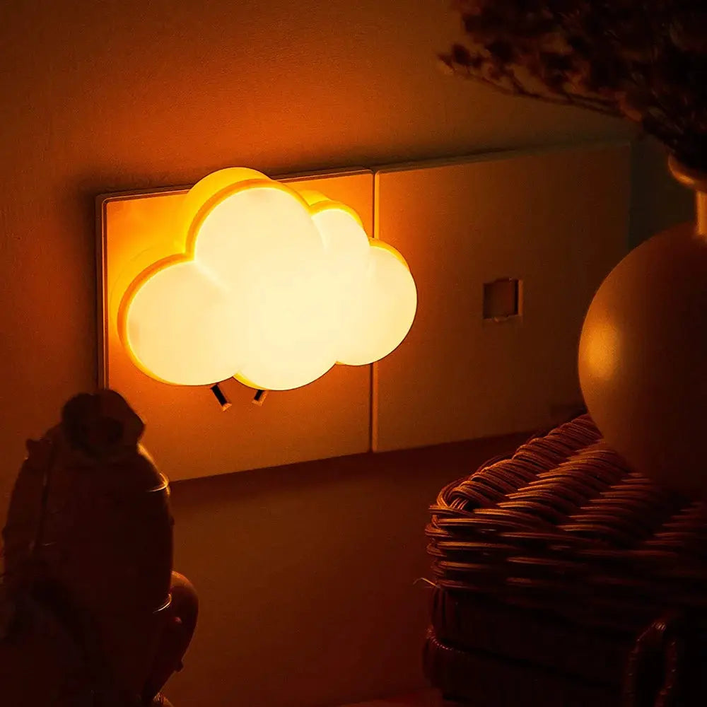 Cloud-shaped LED night light plug-in with warm amber glow plugged into a wall outlet