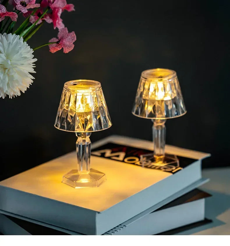 Two mini crystal table lamps with faceted shades and clear stems, warm LED light on books
