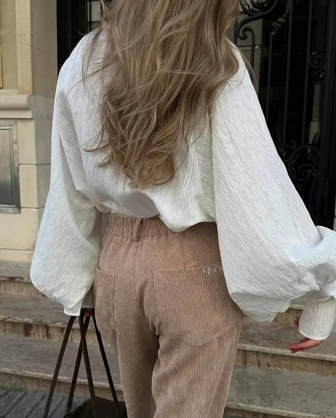 Oversize white cotton shirt for women with long sleeves and minimalist button-up style, paired with tan corduroy pants.