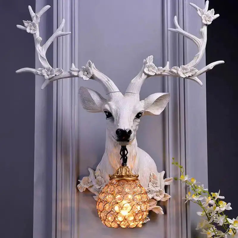 White resin deer wall lamp with flower-adorned antlers and amber globe light fixture