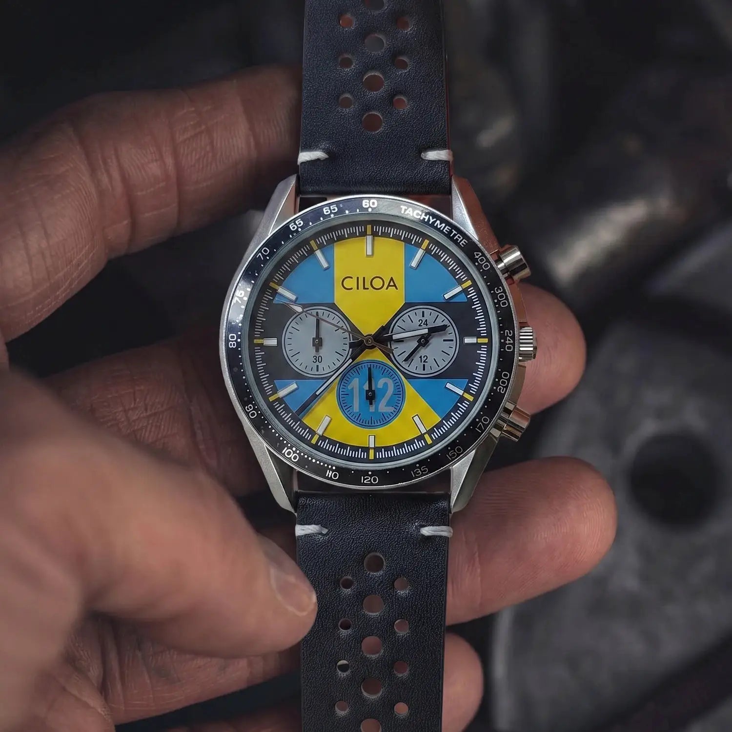 CILOA racing chronograph quartz watch with blue and yellow dial, tachymeter bezel, black perforated leather strap.