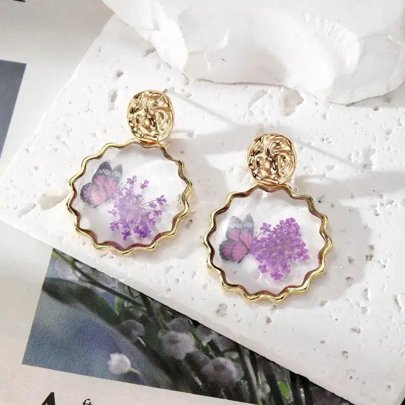 Pair of pressed flower epoxy resin dangle earrings with gold scalloped hoops and purple floral design