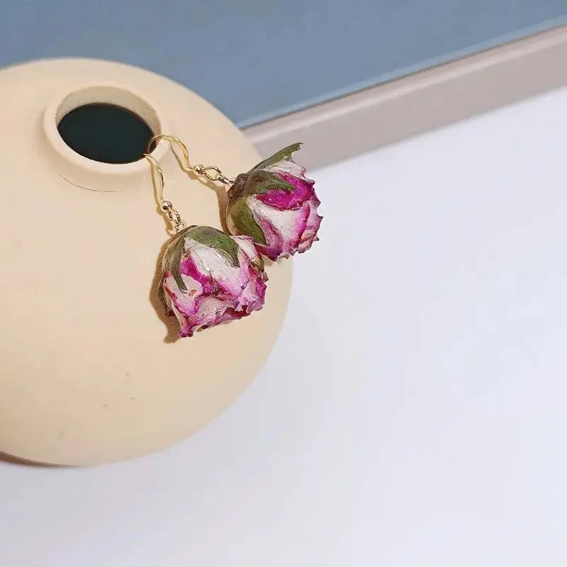 Pair of red rose epoxy resin drop earrings with natural rose buds on gold-tone hooks